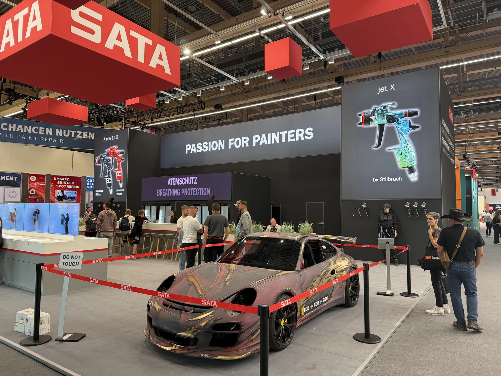 Stoisko SATA na Automechanika Frankfurt 2026 z hasłem „Passion for painters” i samochodem o efektownym lakierze za czerwoną taśmą